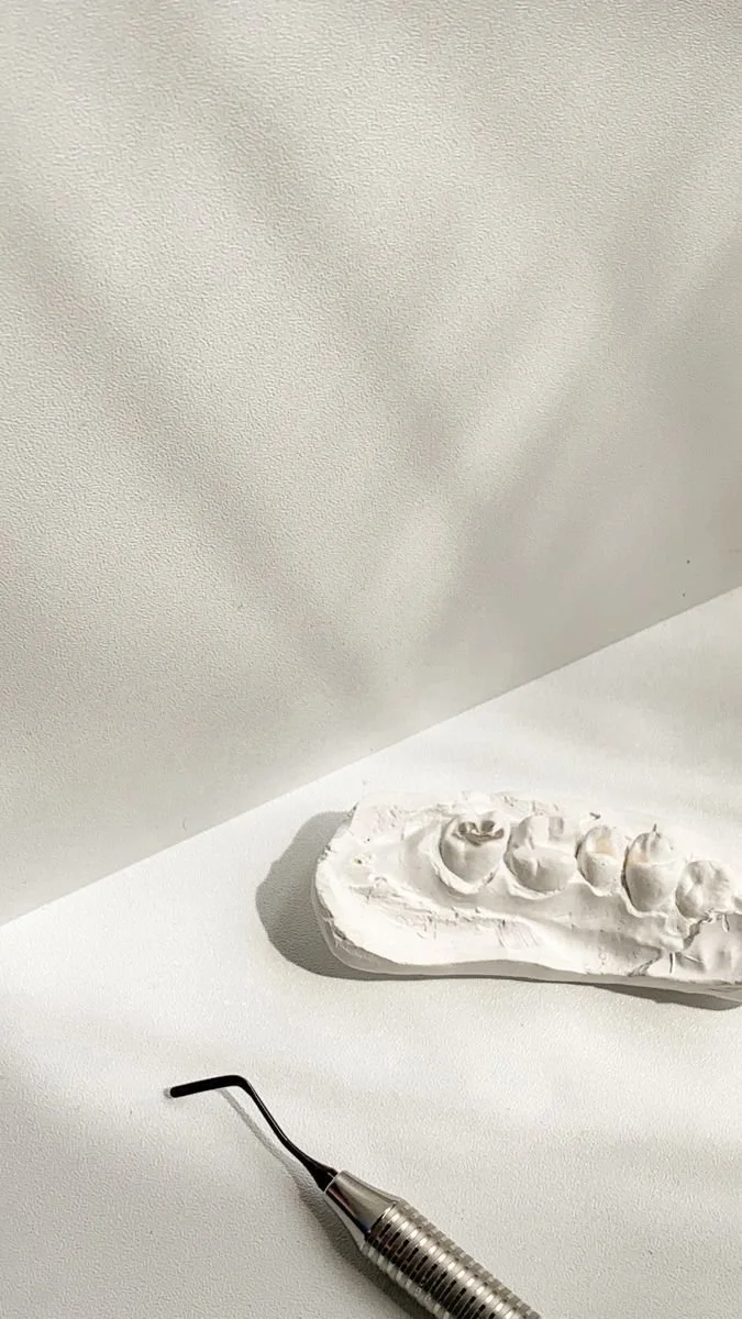 Modelo de silicone dentário branco com alguns dentes feitos e uma ferramenta de pontas curvas ao lado sobre uma mesa