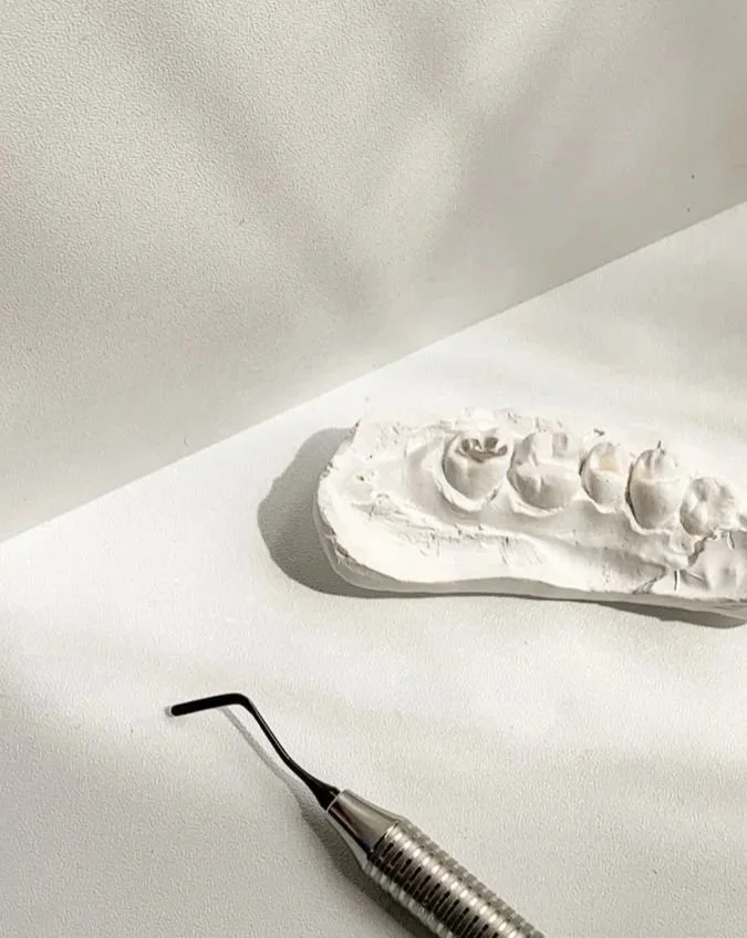 Imagem de uma moldadora de dentes de porcelana em uma mesa branca, com um molde de dentes ao fundo.