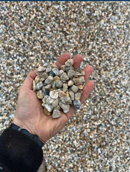 A hand holding small gray and beige rocks with a background of more rocks on the ground.