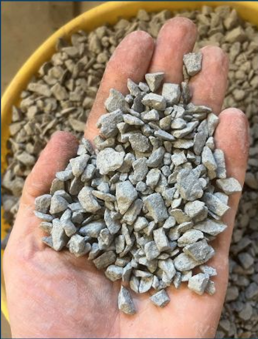A close-up of a hand holding small gray gravel stones, with a yellow container of similar stones in the background.