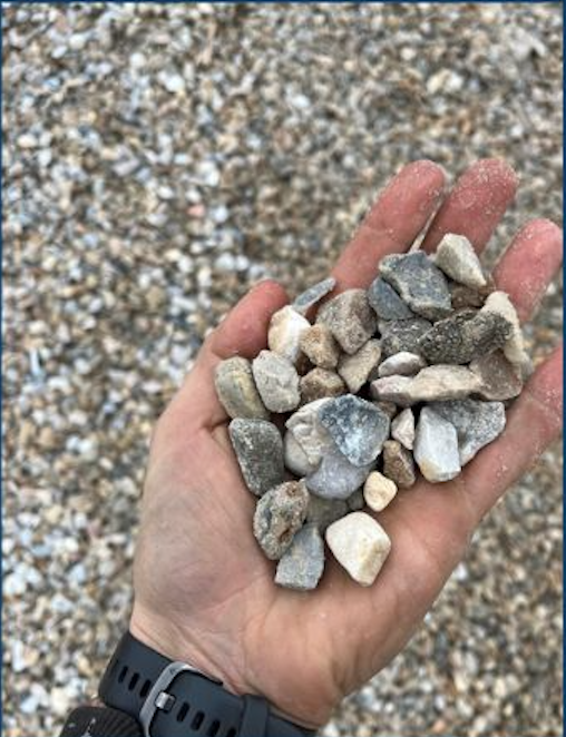 A person's hand holding a handful of small rocks and pebbles with a gravel surface in the background.