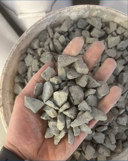 A person's hand holding small gray gravel stones over a larger container of similar stones.