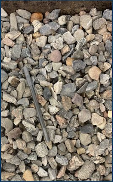 A pile of mixed small rocks and gravel with a metal pen resting among them.