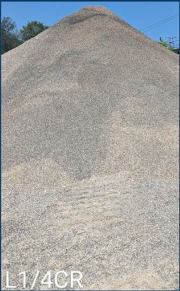 A large pile of gray gravel or sand outdoors with a clear blue sky overhead.