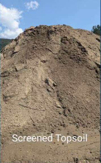 A large pile of screened topsoil outdoors with a blue sky and clouds in the background.