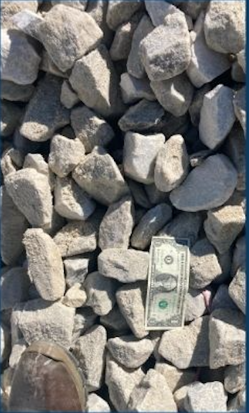 A pile of gray rocks or concrete chunks with a one-dollar bill among them.