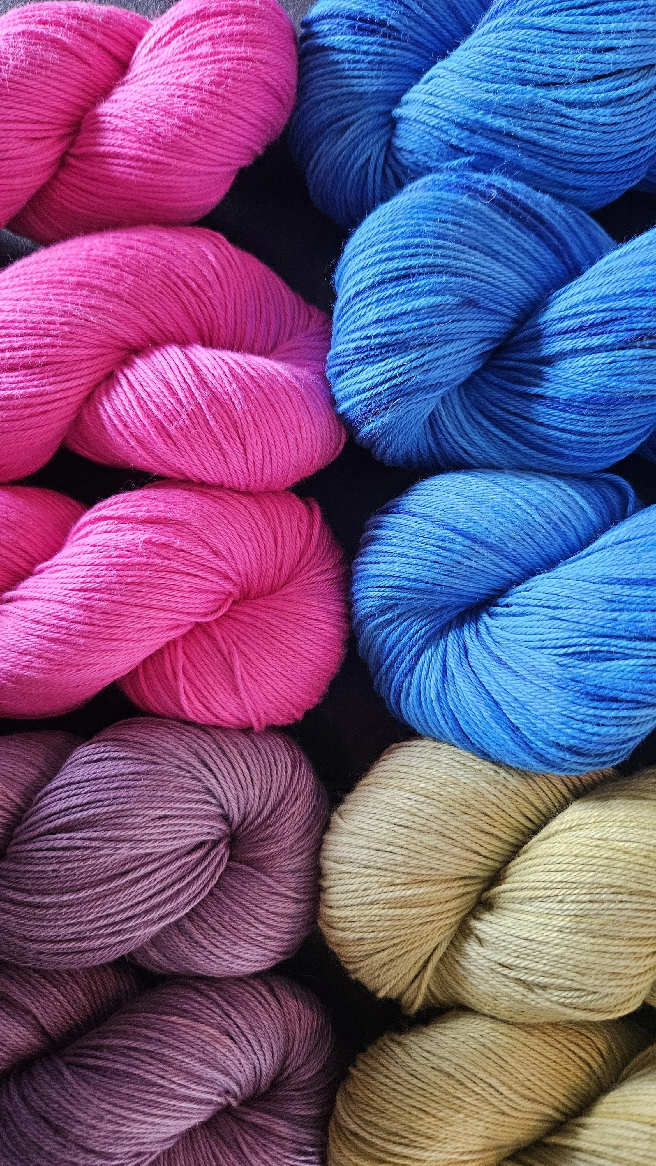 Close-up of colorful skeins of yarn in pink, blue, purple, and beige, arranged in a pattern.