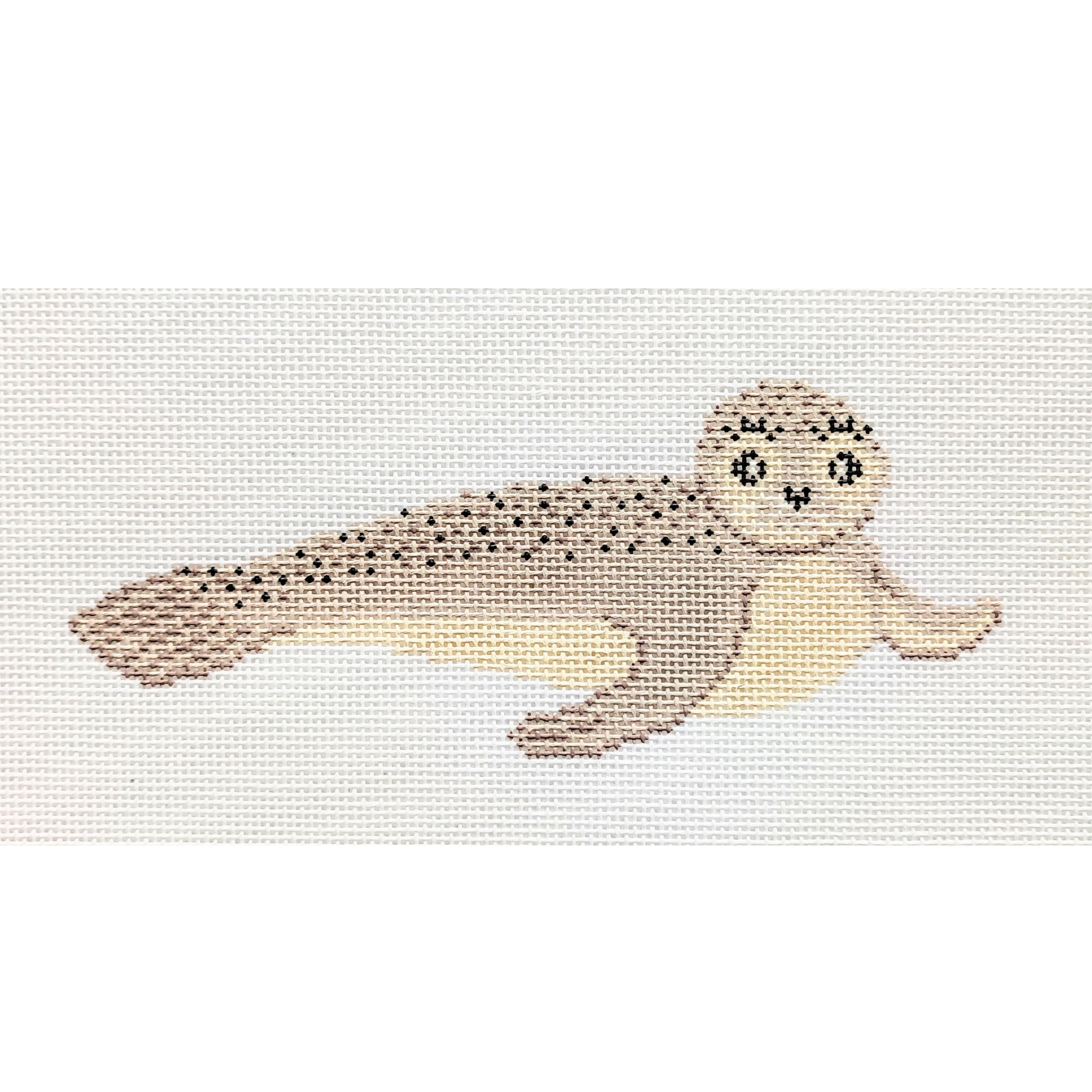Needlepoint design of a cute seal with a light beige body, darker spots, and a happy facial expression, on a white fabric background.