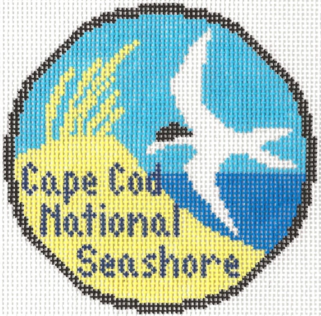 Circular needlepoint design with a blue background, white bird, yellow sky with clouds, and the text 'Cape Cod National Seashore"