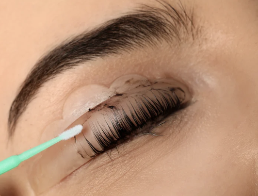 Close-up of an eye with lengthy eyelashes, with a cotton swab applying eyelash adhesive or serum.