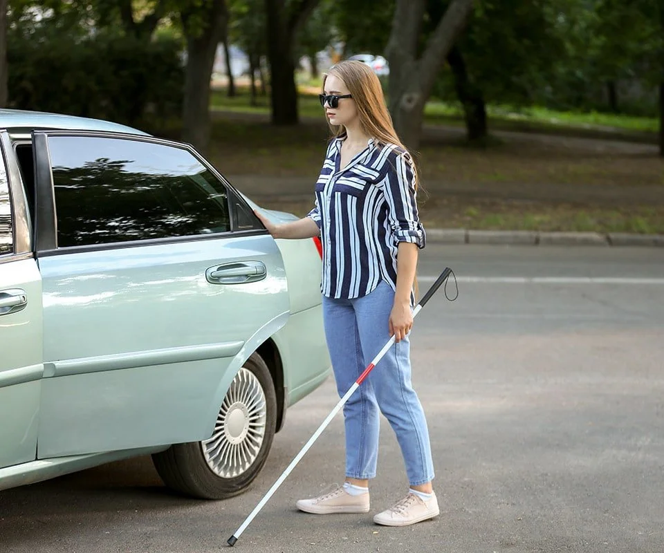 Blind woman in jeans and a striped shirt getting into a car.