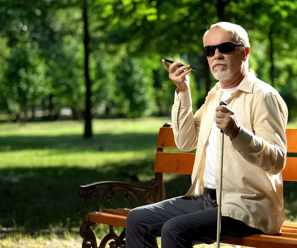 Blind man sitting on a park bench using a cell phone