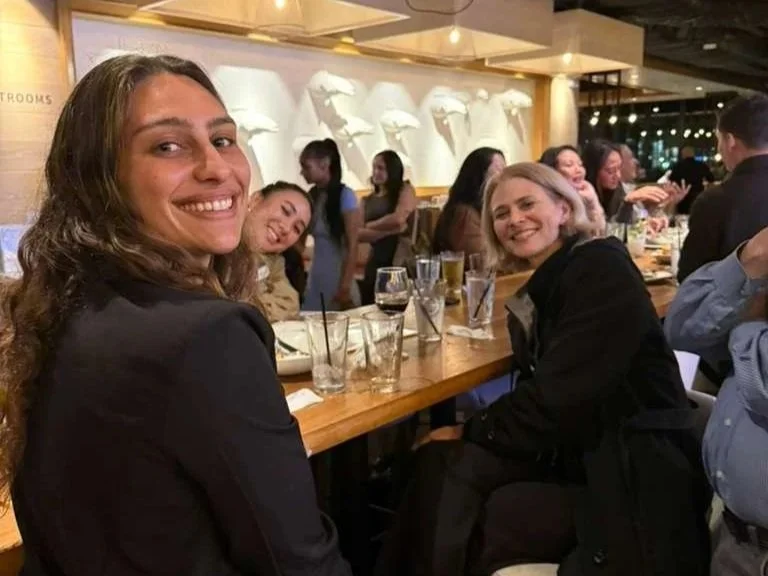 Smiling group of women enjoying drinks at a bar or restaurant, with a wooden counter, glasses, and group conversation.