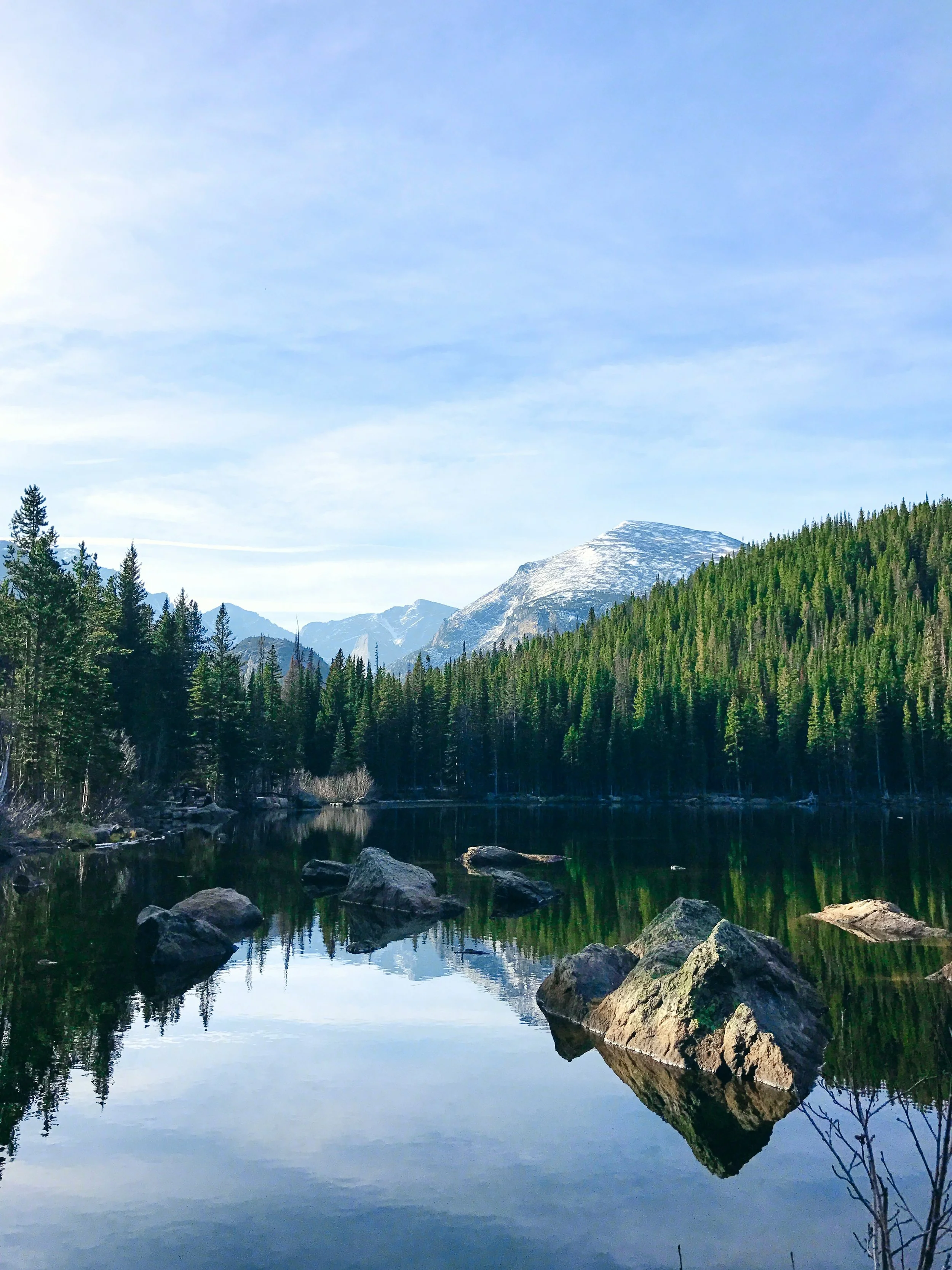 A tranquil mountain lake with reflection of surrounding trees and snow-capped mountains in the background under a clear blue sky.