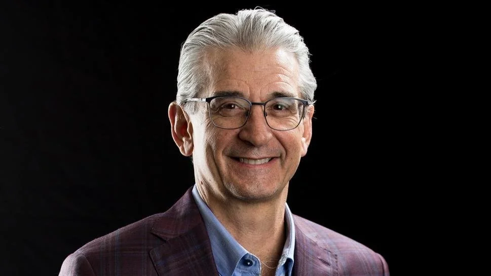 Smiling older man with glasses and gray hair against a black background