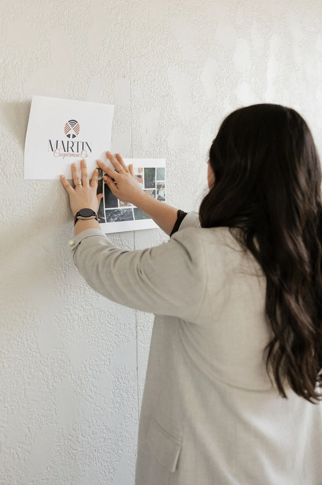 A woman hanging a printed sign that reads 'MARTIN Cooperman Co' on a textured white wall.