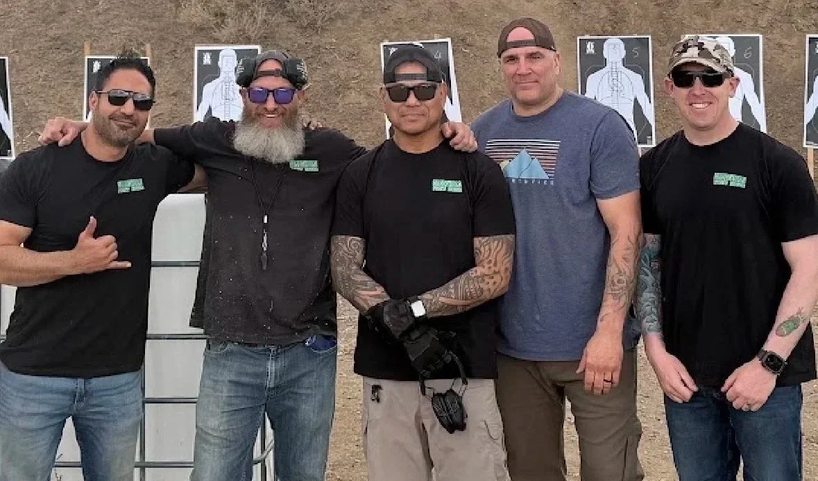 Combatives instructors teaching together outdoors, at a target shooting range, with target silhouettes in the background.