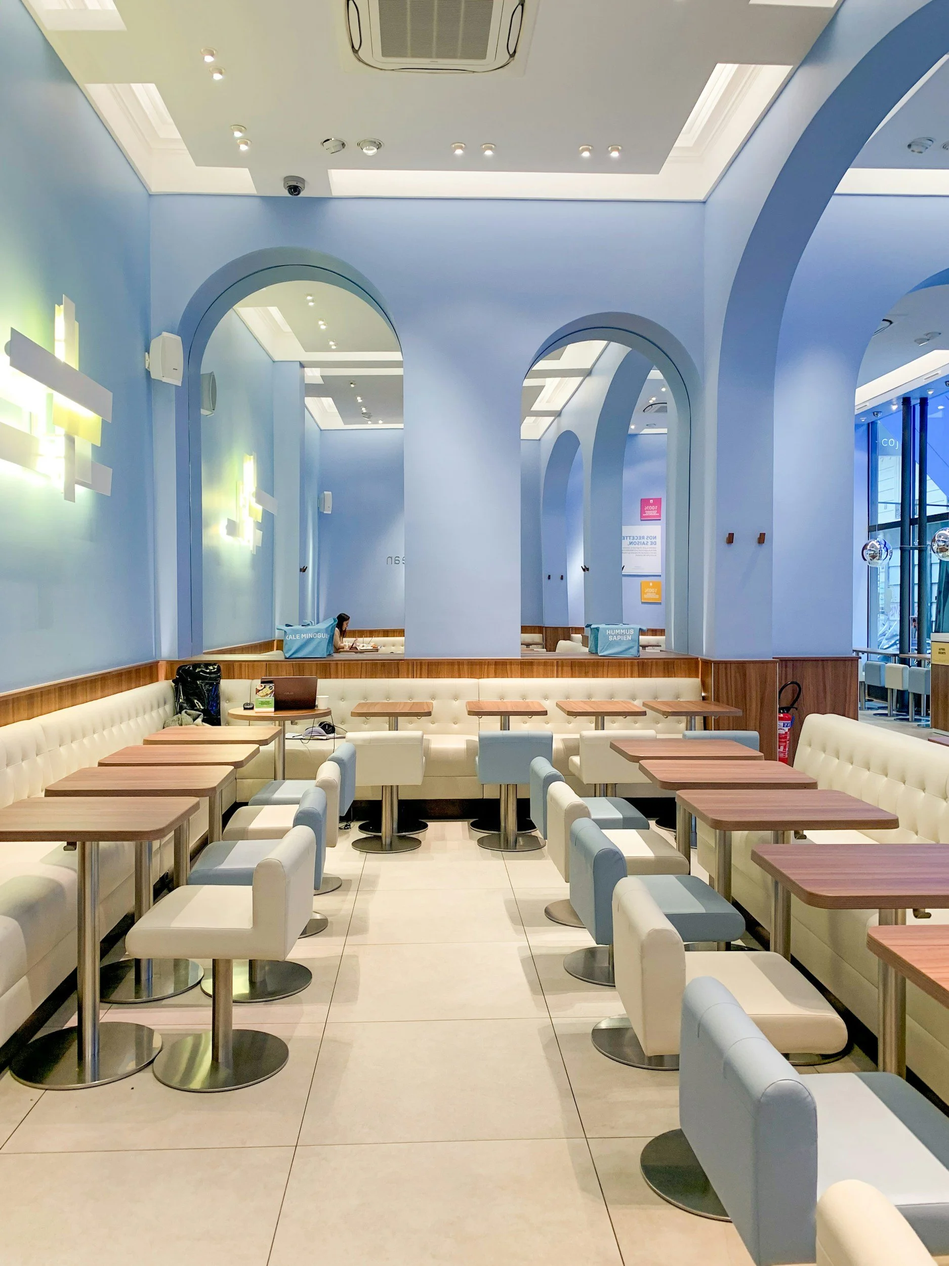 Empty modern restaurant interior with white and light blue chairs, wooden tables, blue walls, and arched openings.