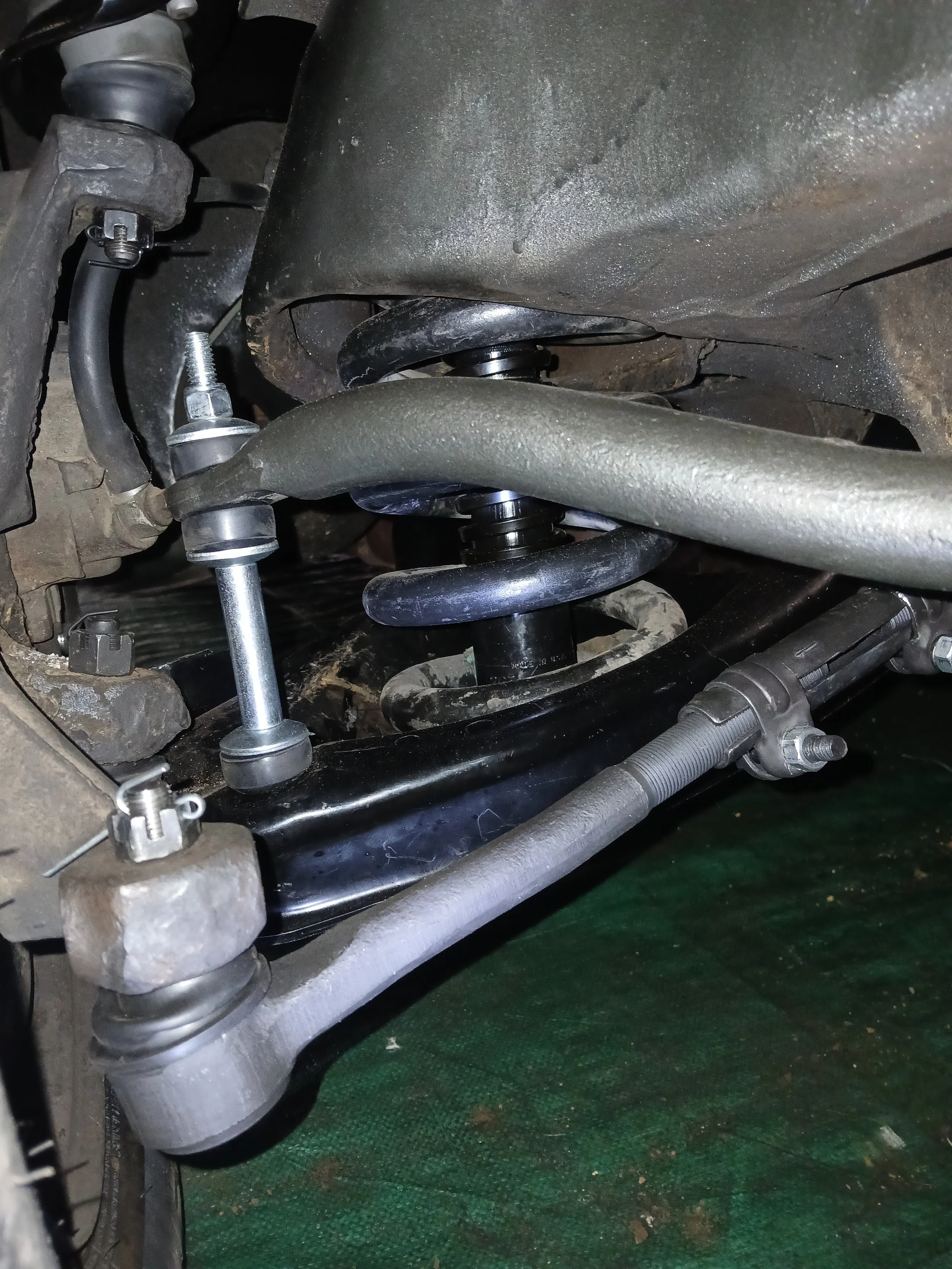Close-up view of a vehicle suspension system showing shock absorber, coil spring, control arm, and stabilizer bar.