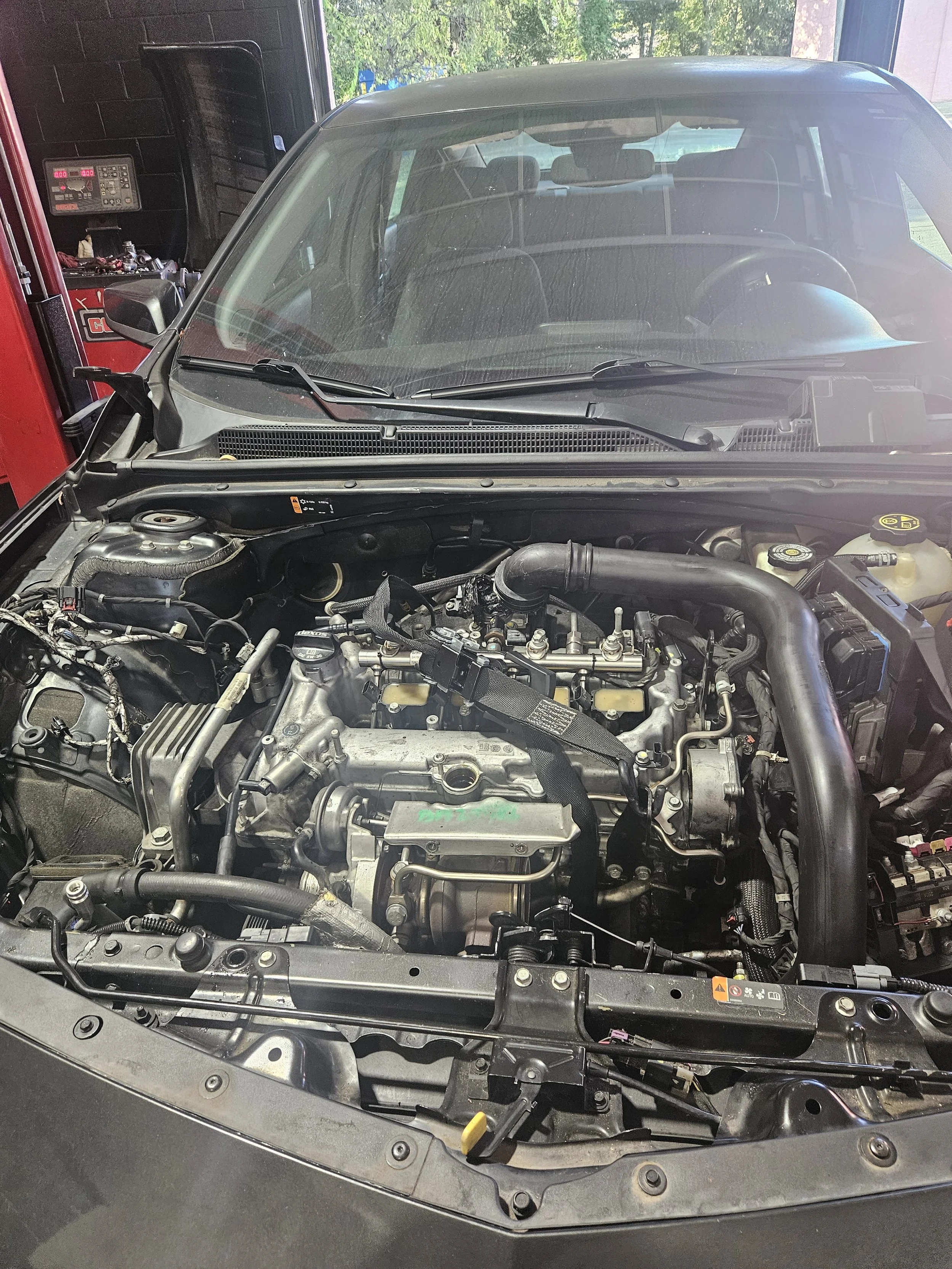 Car with hood open showing engine in a garage or workshop.