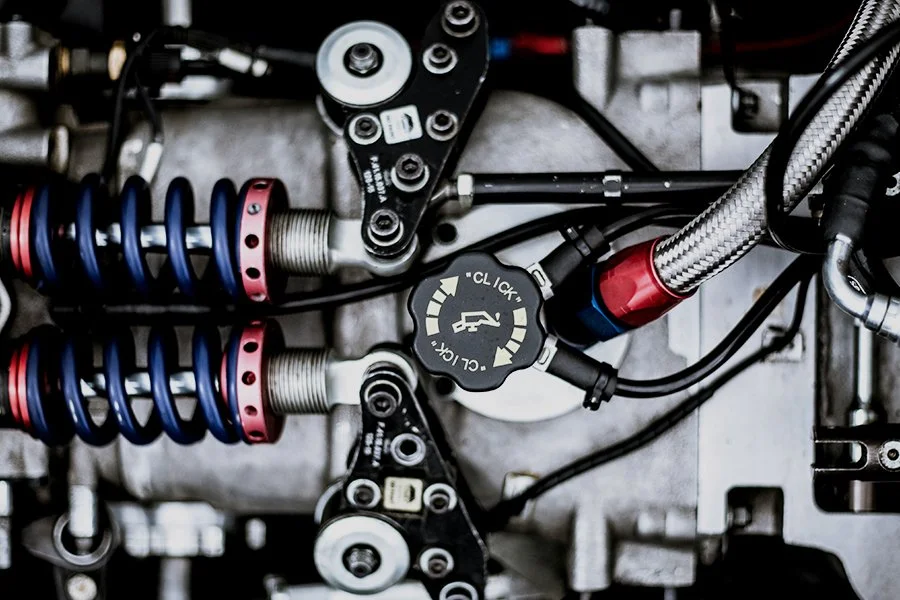 Close-up of automotive suspension and steering components, including coil springs, shock absorbers, and a power steering fluid cap.