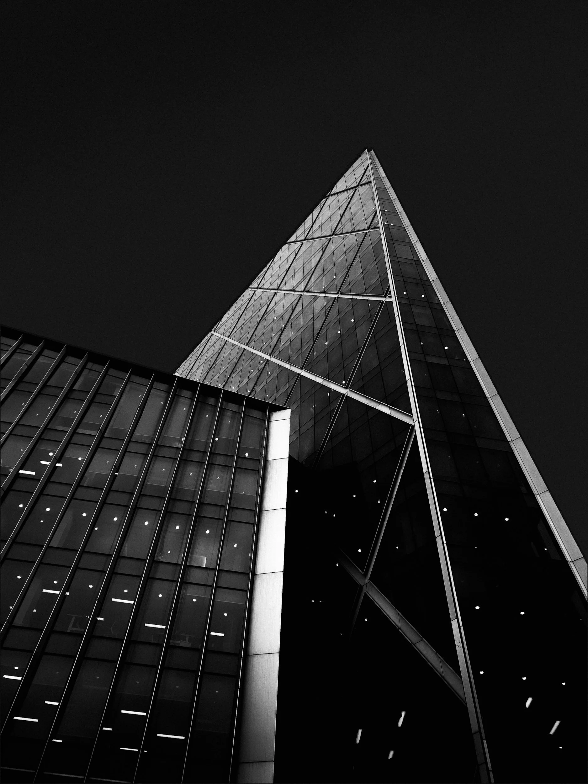 A modern, glass skyscraper at night with sharp angles and illuminated windows against a dark sky.