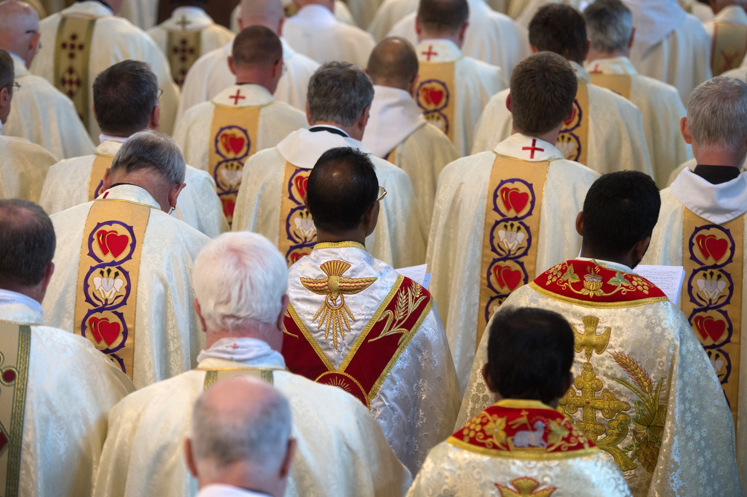 A large group of priests and clergy dressed in ornate white and red vestments, gathered in a Holy Mass