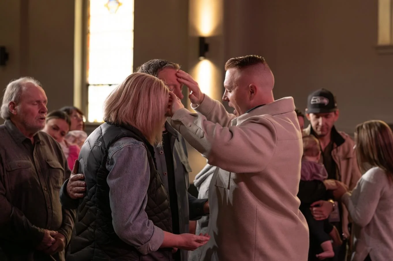 A scene in a church with a man praying over a woman who is crying, surrounded by other people praying or observing.