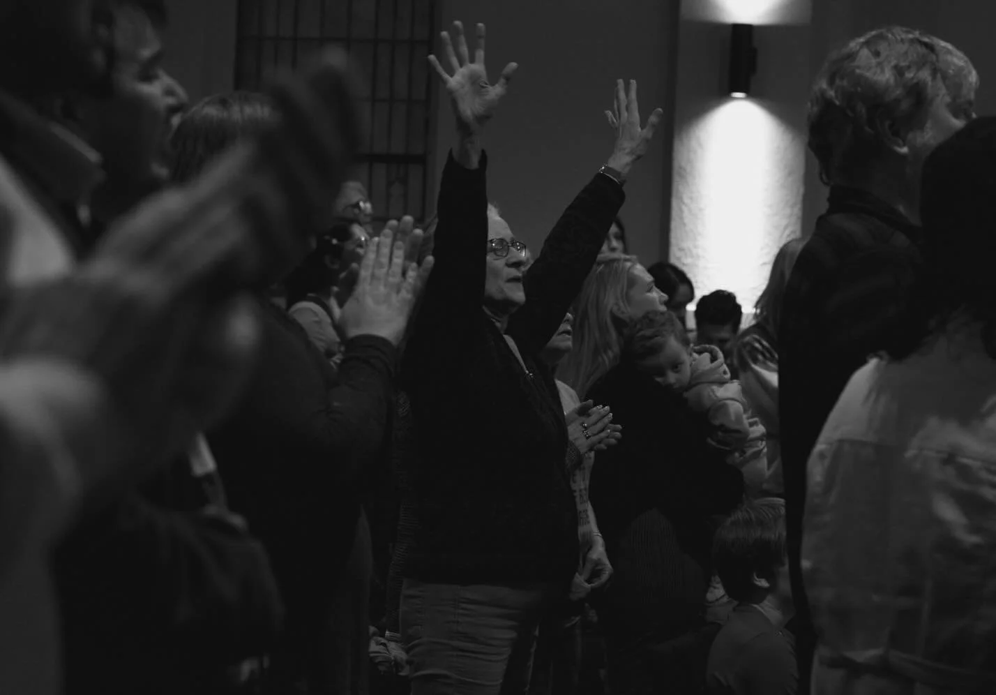 People in a congregation with some raising their hands and others clapping, in a church or worship setting.