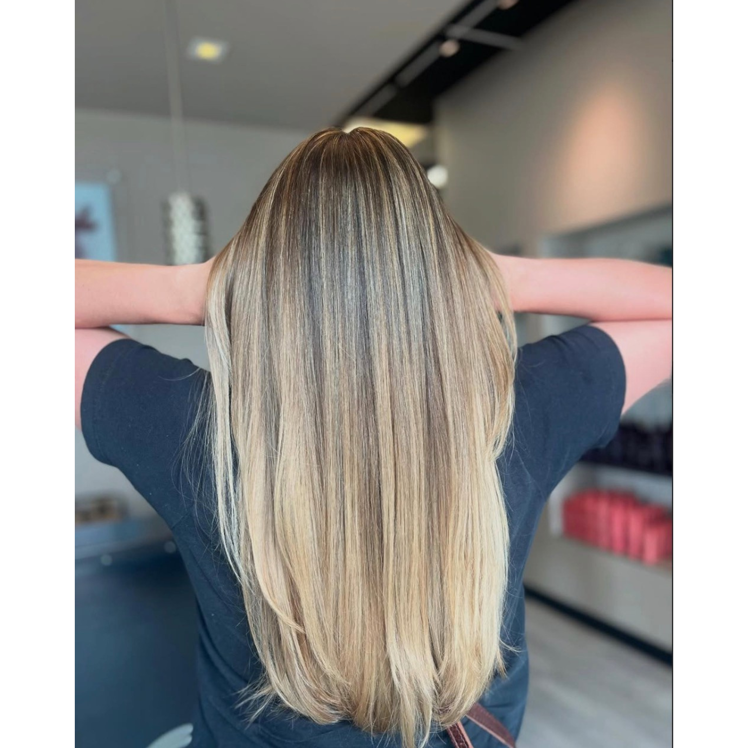 Back view of a woman with long, straight, blonde hair in a salon setting.