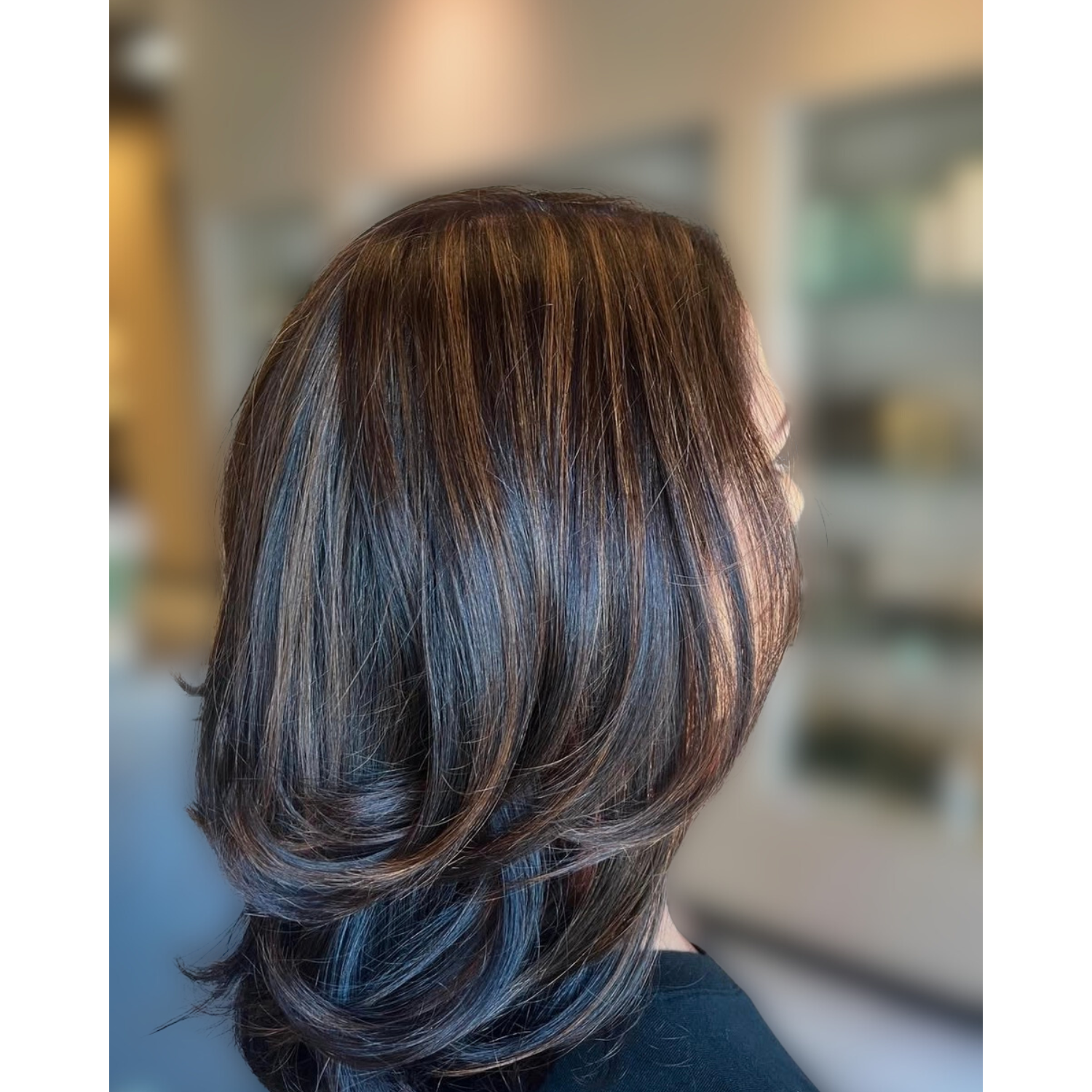 Side view of a woman with shoulder-length, layered brown hair with highlights, indoors.