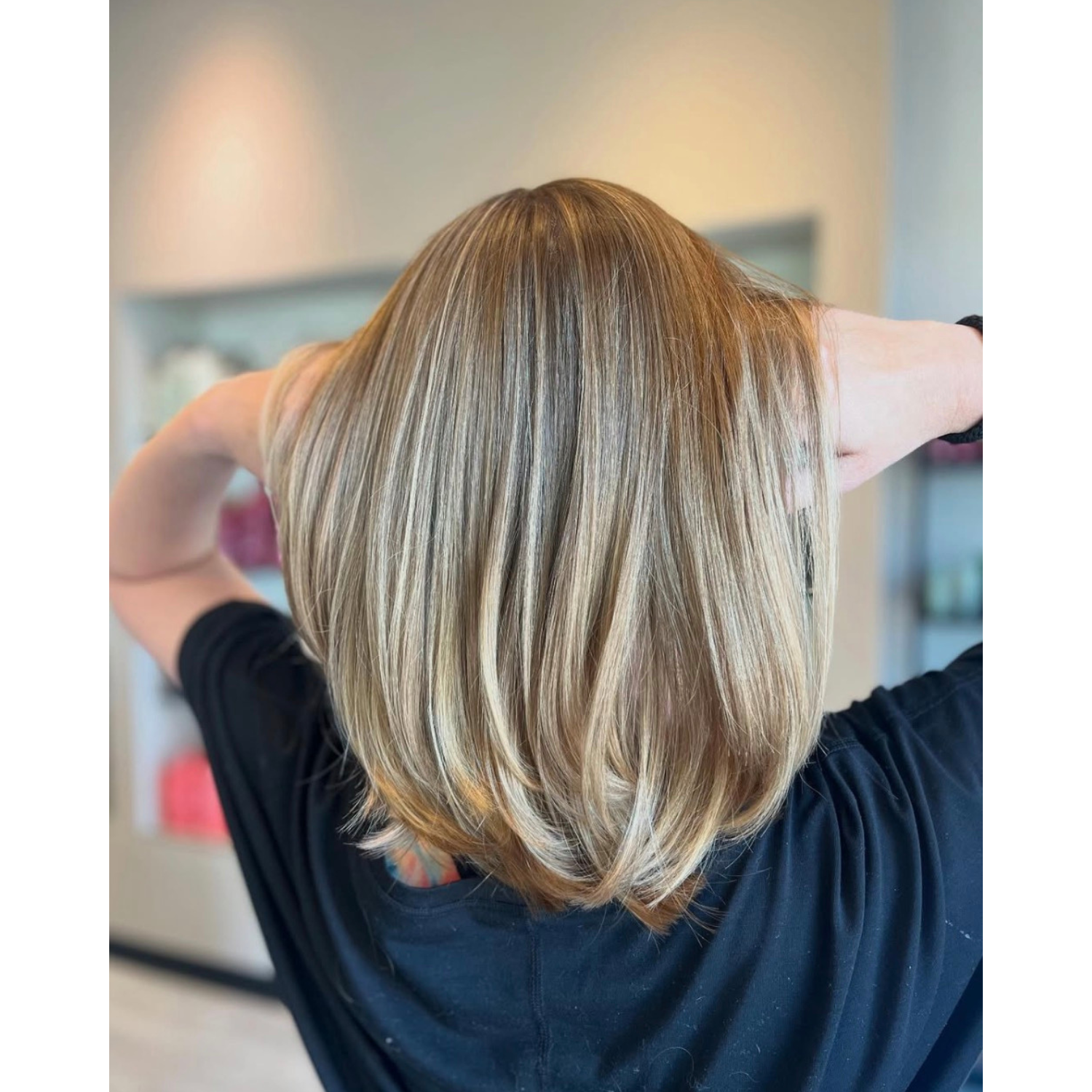 Woman with shoulder-length, blonde hair, seen from behind, in a salon or similar setting.