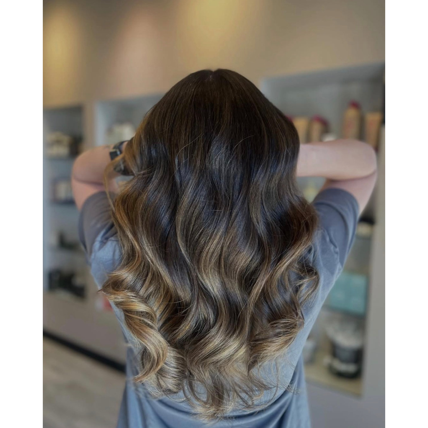 Back view of a woman with long, wavy hair that transitions from dark brown at the roots to blonde at the ends.
