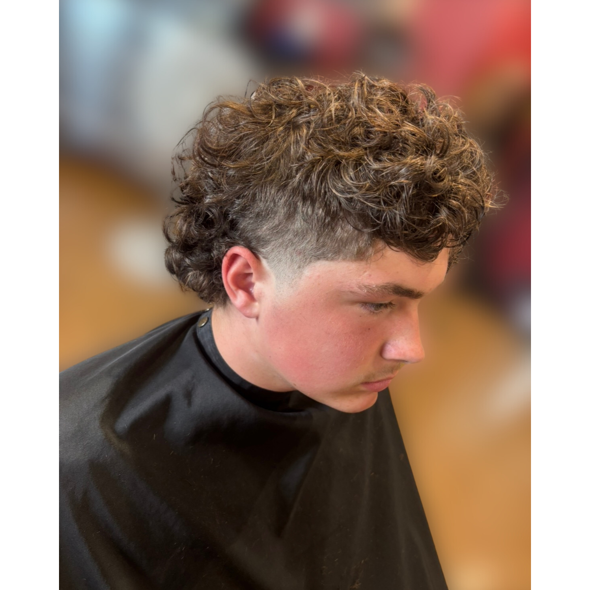 Young person with curly hair getting a haircut at a salon, wearing a black cape.