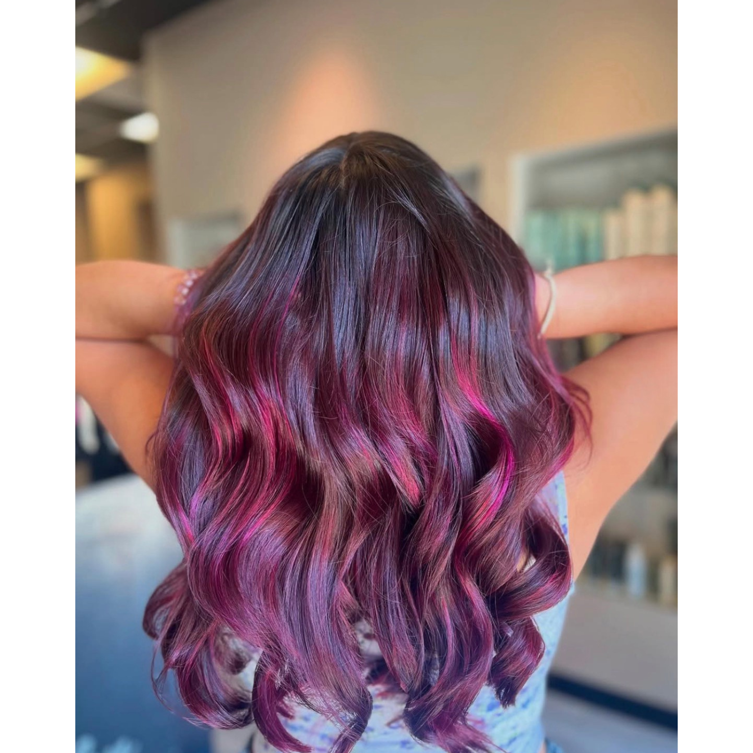 Back view of a woman with long wavy hair dyed in shades of pink and purple.