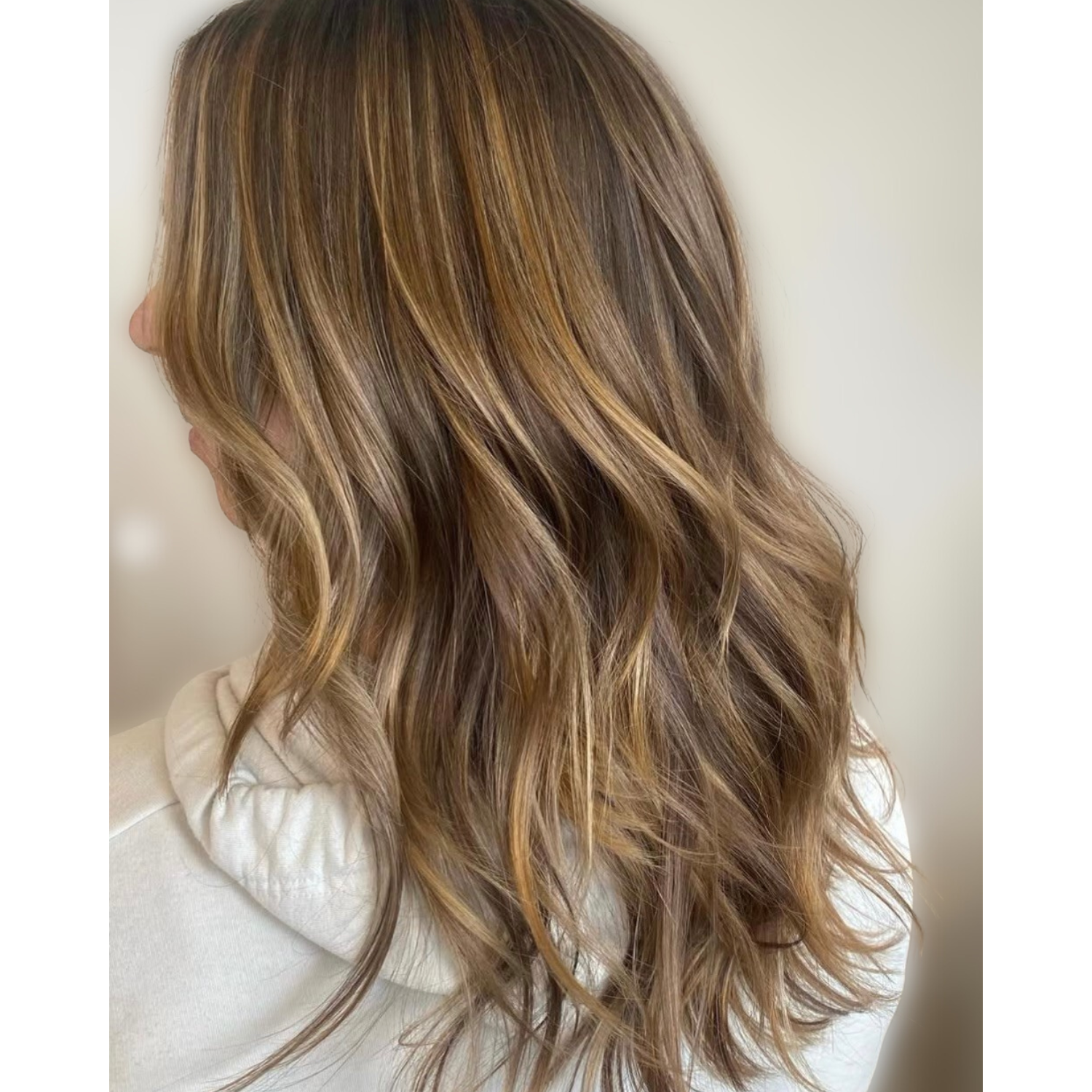 Side view of a woman with long, wavy, ombré hair starting with darker roots and transitioning to lighter ends.
