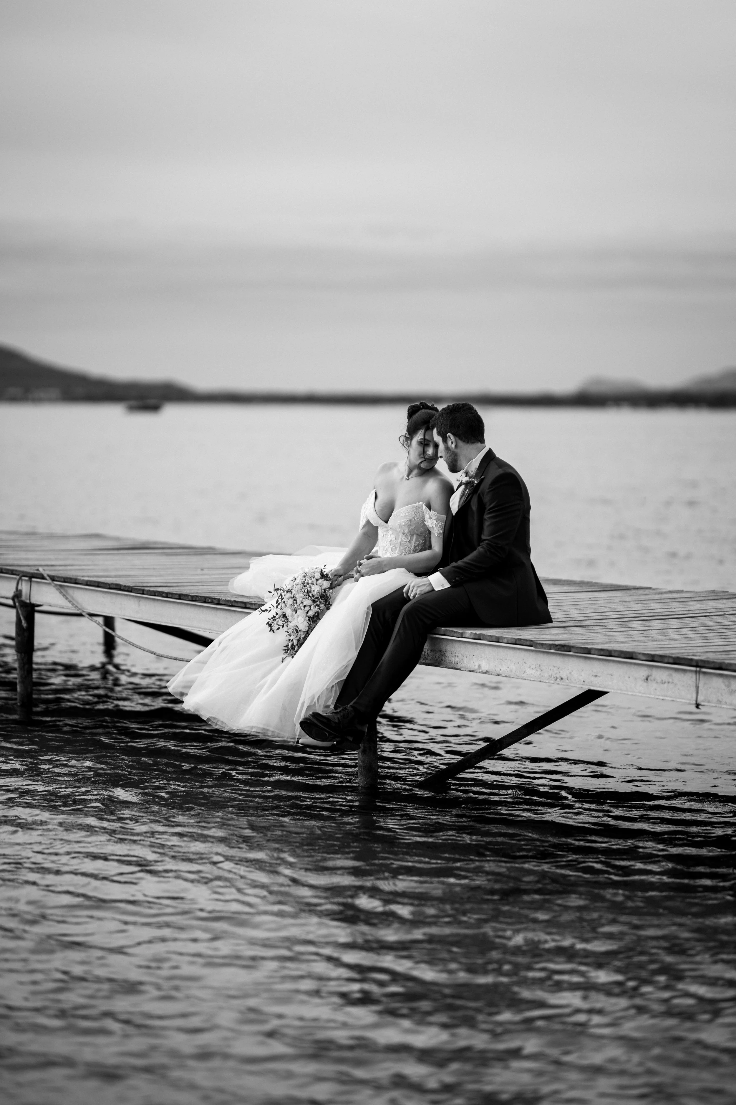Sposi seduti sul pontile sul mare in bianco e nero.