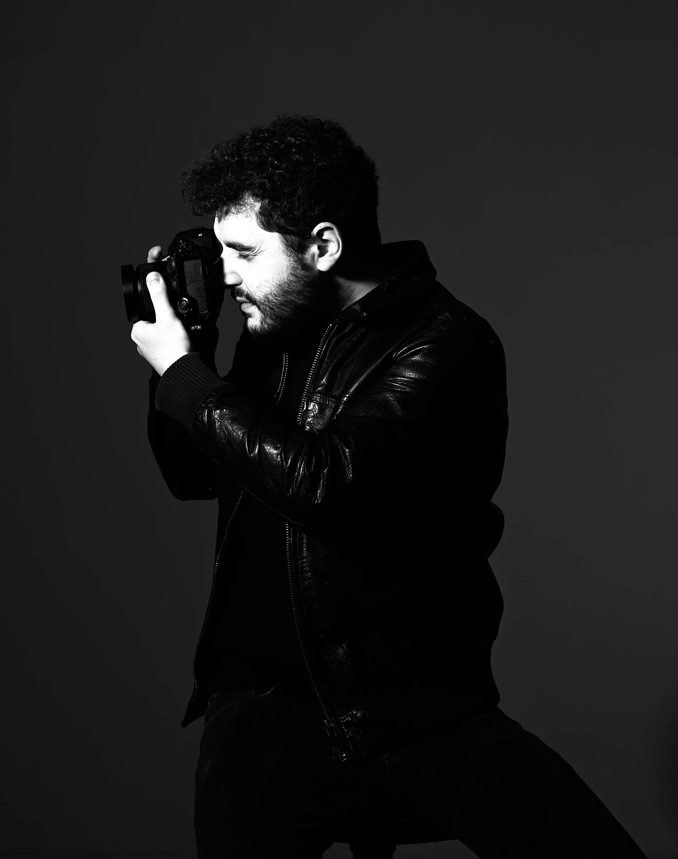 Ritratto in bianco e nero di Angelo Meloni mentre fotografa con una macchina professionale.