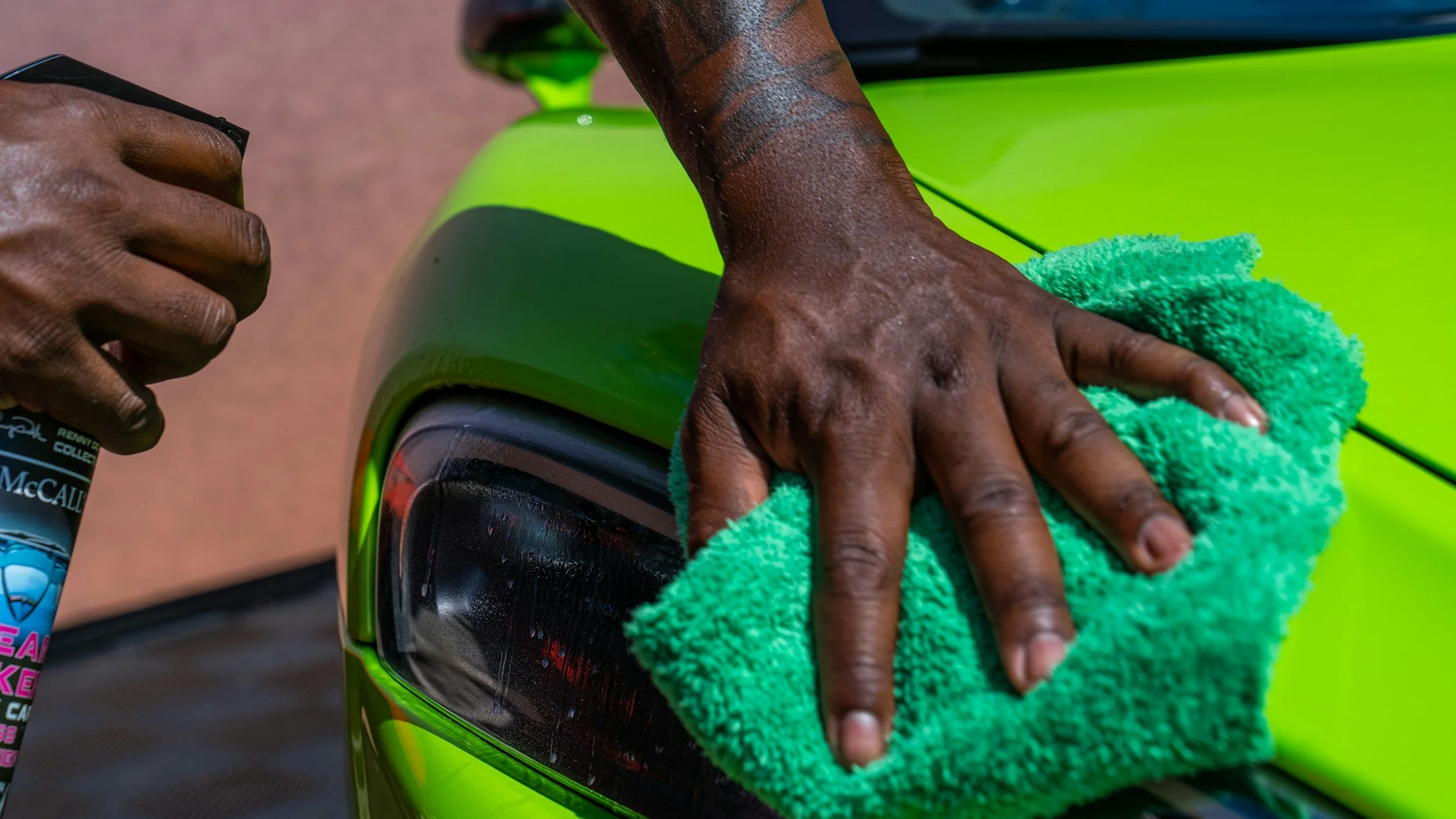 Close-up of a person cleaning a bright green car with a green microfiber cloth.