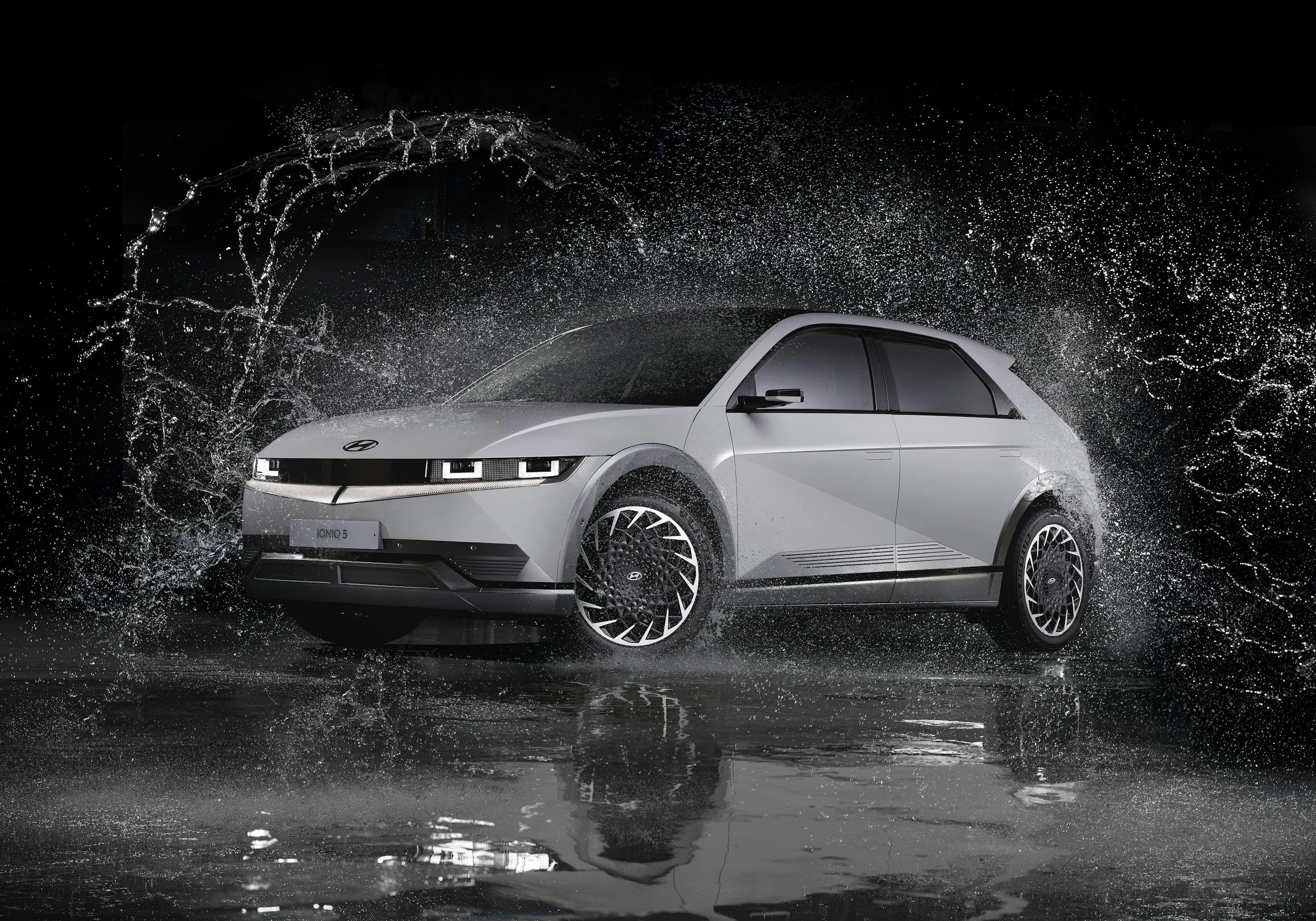 A silver Hyundai Ioniq 5 electric car on a wet surface with water splashing around in a dark setting, showcasing a modern and futuristic design.