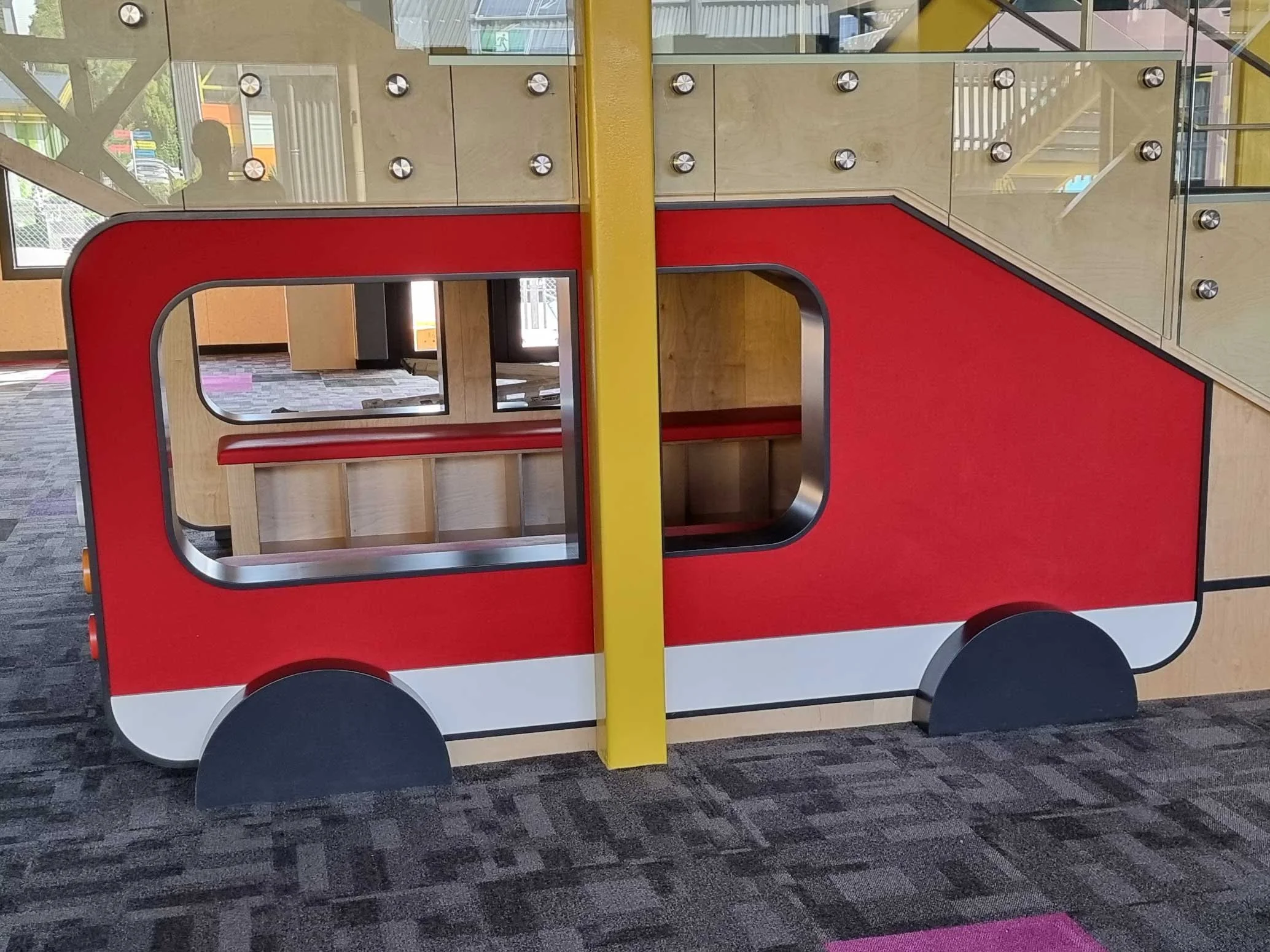 Child's playhouse designed to look like a fire truck, made of wood with red, yellow, black, and white coloring, situated inside a fire station or playground.