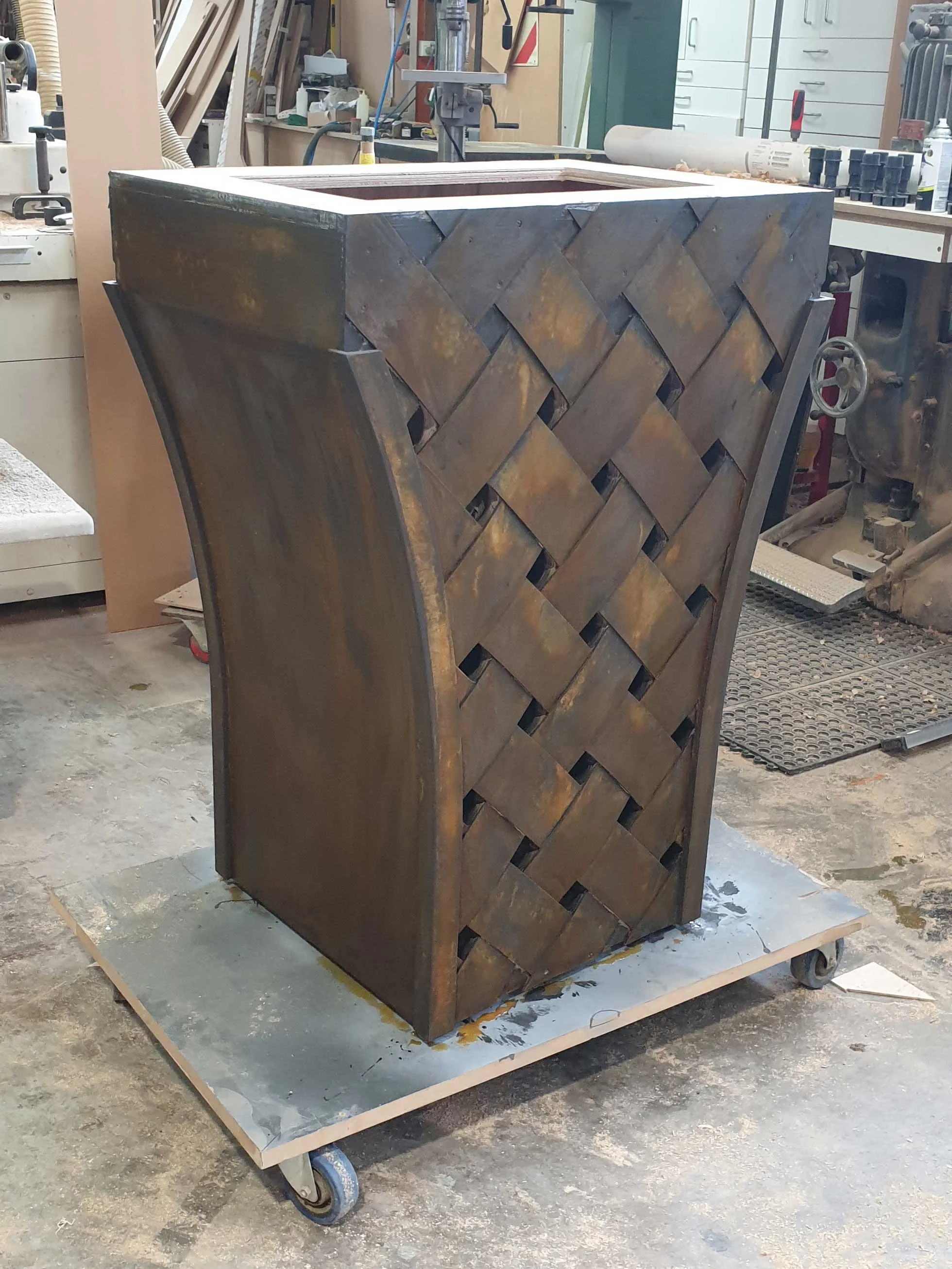 A wooden cabinet with a woven pattern on the front, unfinished and in a workshop.