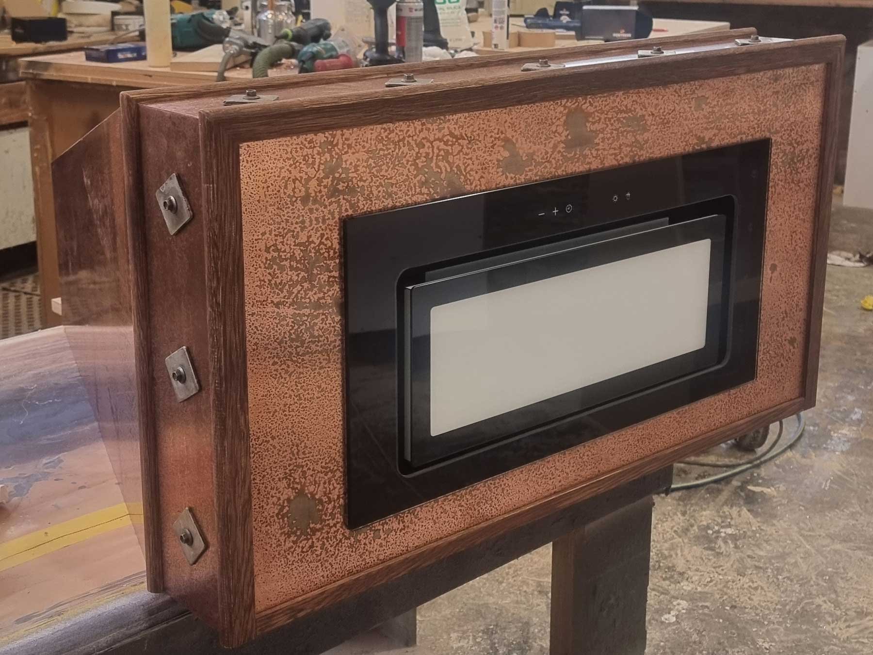 Wooden cabinet with a black framed white microwave, mounted on a stand in a workshop.