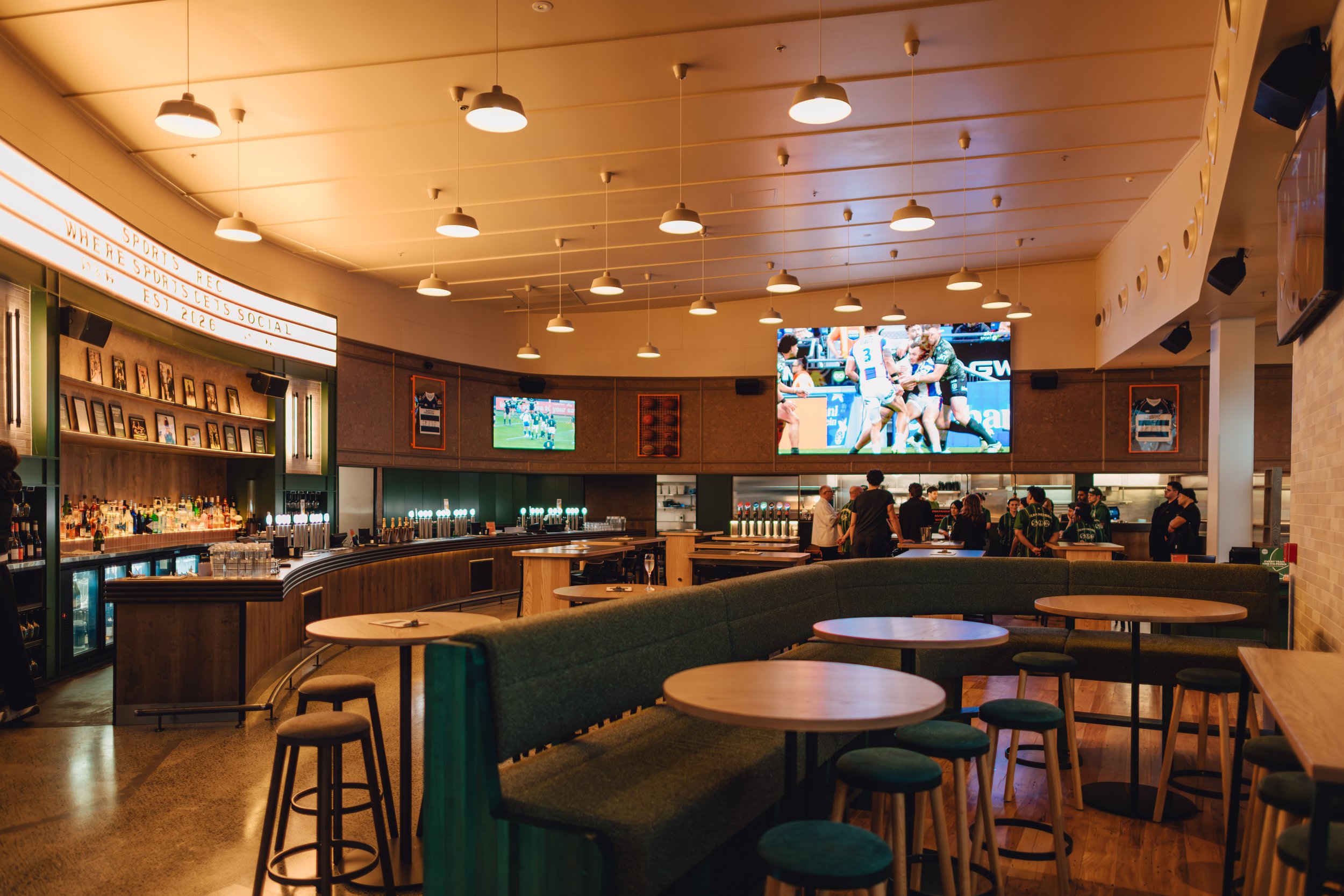 Wide interior shot of Sports & Rec Bar showcasing the completed curved bar counter, timber ceiling panelling, custom joinery and LED screen wall.