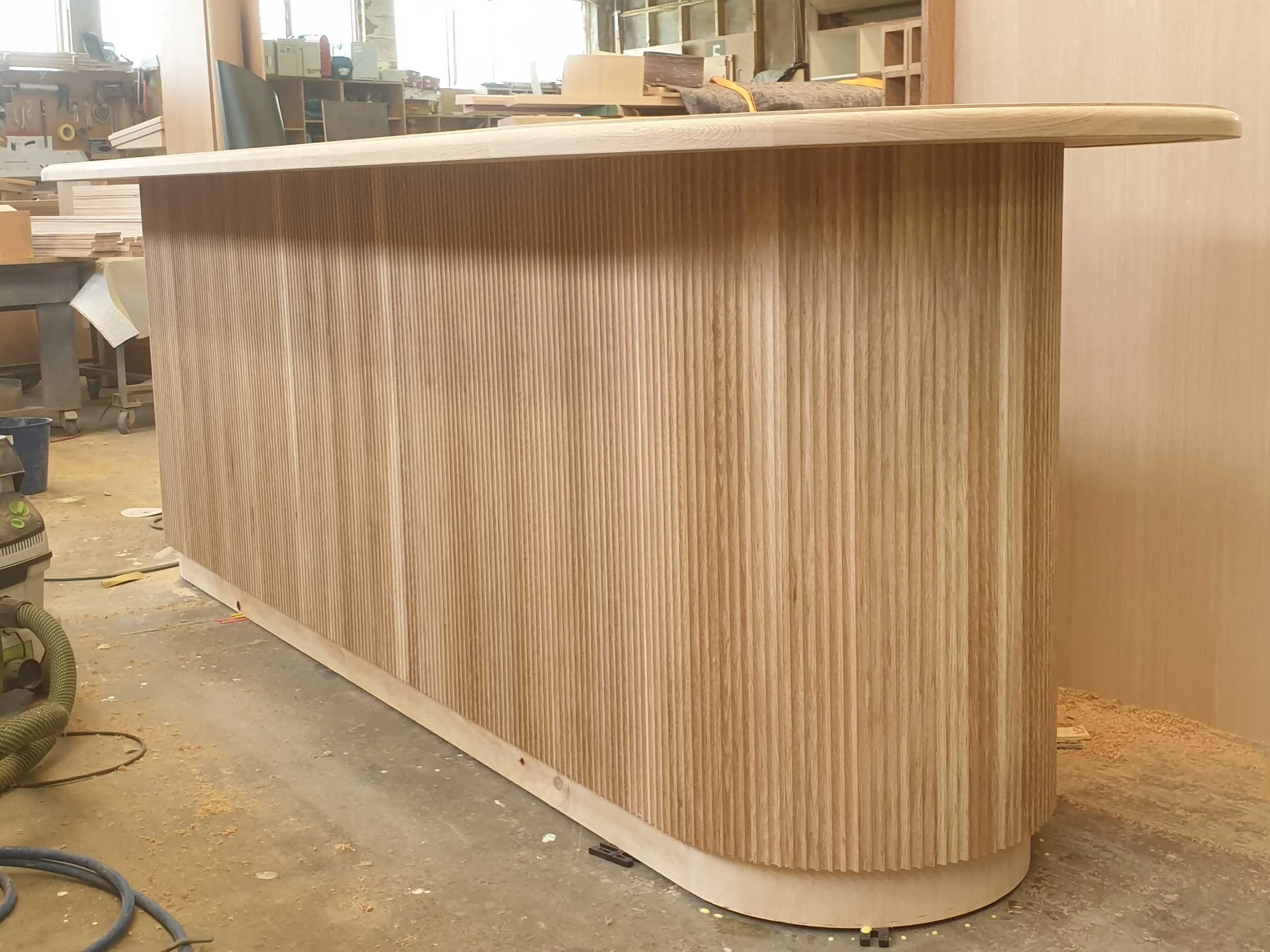 A wooden bar counter with vertically ribbed paneling, situated in a woodworking shop.