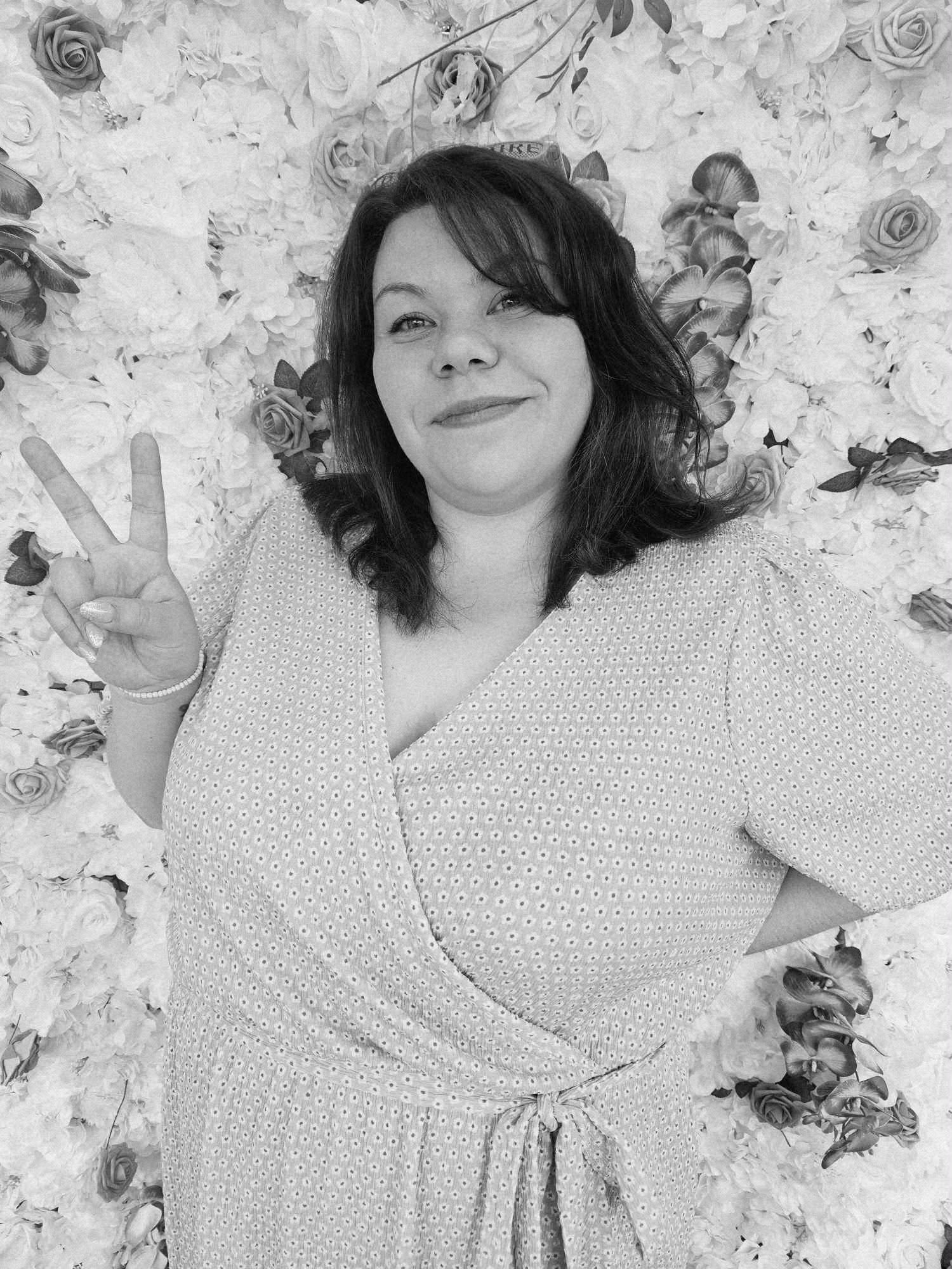 A man sitting on a cushioned bench against a plain beige wall, wearing a blue short-sleeve sweater and beige pants, looking to the side with a neutral expression.