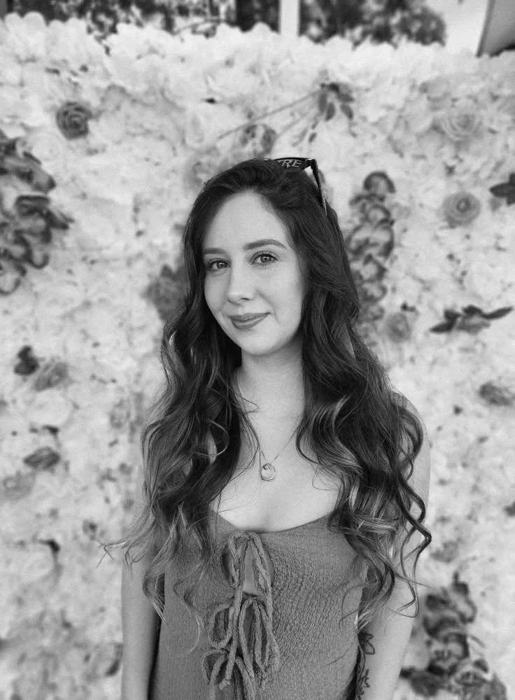 Young man sitting on a bench against a neutral wall, wearing a gray polo shirt and light-colored pants, casting a shadow on the wall.