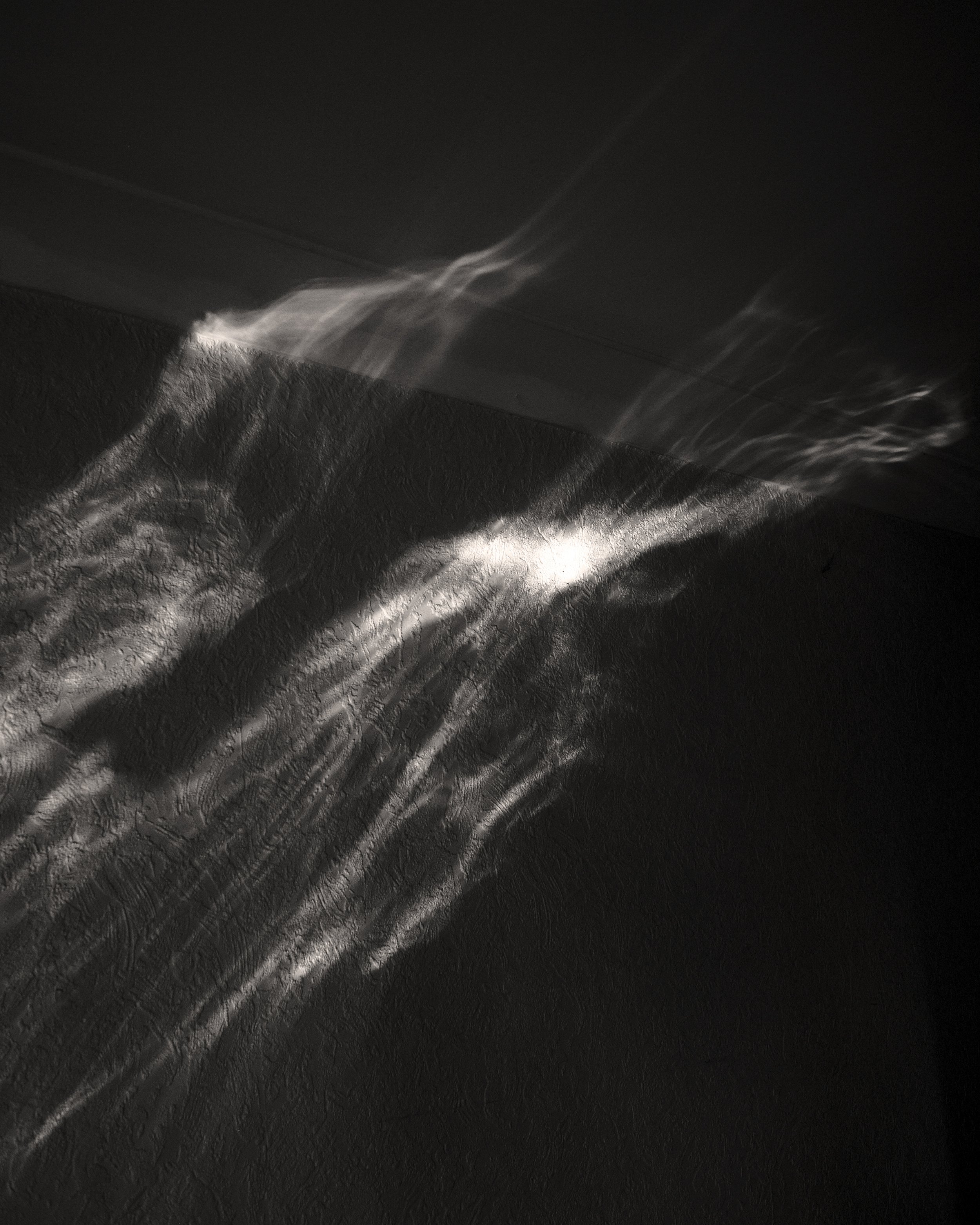 Light passing through a curtain, creating reflections on a dark textured surface.