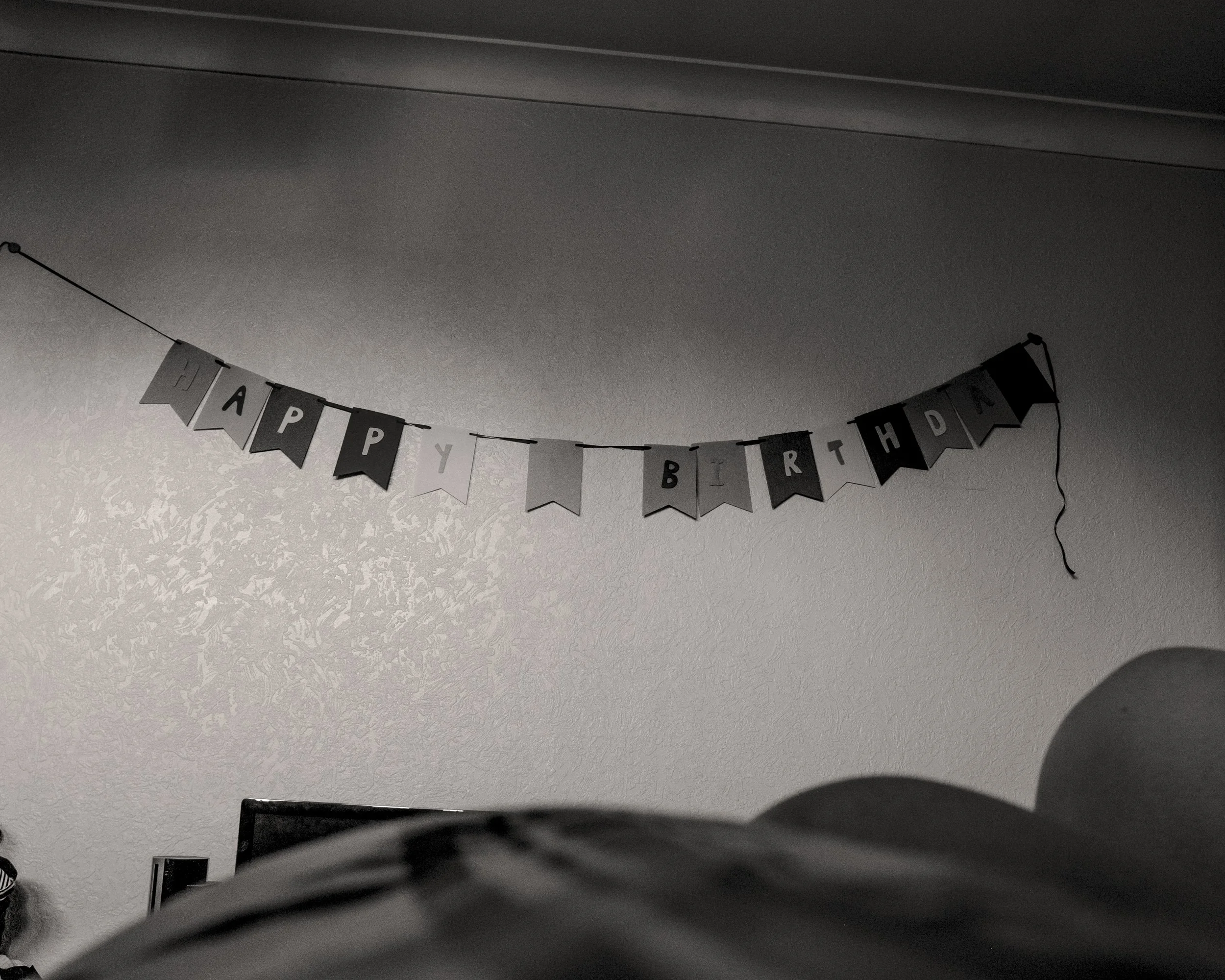 Black and white photo of a 'Happy Birthday' banner hanging on a wall in a room.