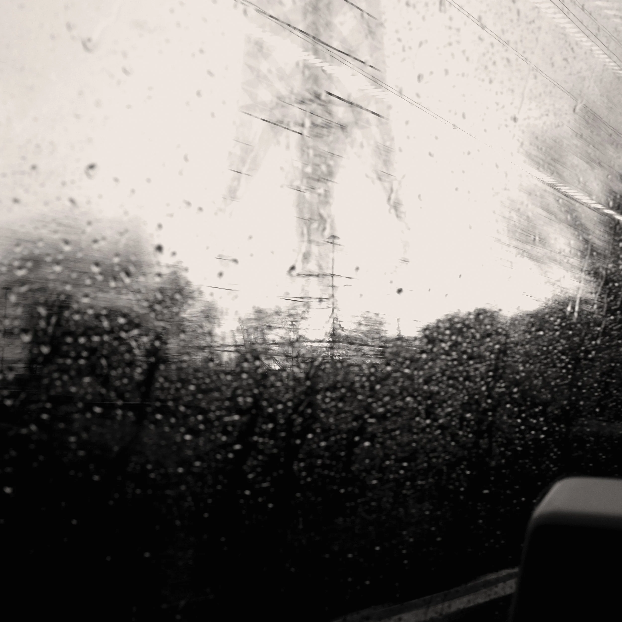 Rainy view through a car window with streaks and raindrops, electrical tower, and trees visible in the distance.